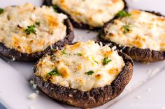 four stuffed mushrooms with cheese and parsley on a white plate, ready to be eaten