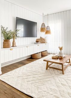 a living room with white walls and wooden floors, large tv on the wall, two planters in vases