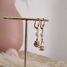 Step into timeless elegance with these dainty and romantic handmade mismatched earrings inspired by Aphrodite, the ancient Greek goddess of love, beauty and desire. The earrings feature a cute seashell charm made of 14k gold plated brass, symbol of the birth of Venus, and a rose stem, the flower associated with the goddess. Two beautifully wrapped freshwater pearls and a pair of shell shaped lever backs complete the design. Handcrafted with the utmost of care, these Aphrodite dangling pearls ear Aphrodite Greek Goddess, Cute Seashell, Artsy Earrings, Ethereal Jewelry, Vintage Gold Earrings, Lotus Earrings, Moon Moon, Rose Stem, Retro Earring