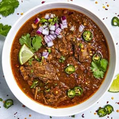 a white bowl filled with meat and vegetables next to cilantro, lime wedges