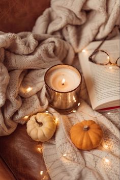 an open book, glasses and pumpkins on a blanket with lights in the background