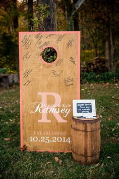 a wooden sign sitting next to a barrel on top of a grass covered field with trees in the background