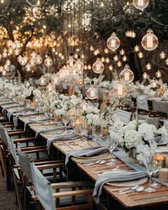 a long table set up with white flowers and hanging lights