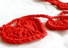 two crocheted red hearts on a white surface with one attached to the other