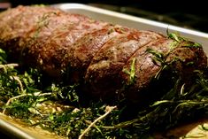 a large piece of meat sitting on top of a pan covered in green leaves and herbs