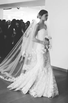 the bride is walking down the aisle in her wedding dress with flowers on it and veil over her head