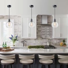 a kitchen with white cabinets and marble counter tops, bar stools and pendant lights hanging from the ceiling