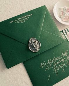 a green envelope with a wax stamp on it next to a cup and saucer