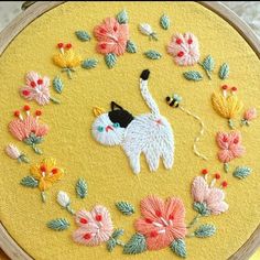 an embroidery kit with flowers and a cat on it's back, sitting in front of a circular frame