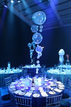 To access the dining area guests made their way through an opulent deep wall of fabric columns, emulating waves and shafts of light in the sea. Dining tables were dressed in four different shades of blue cloths, surrounded with clear perspex chairs. Bubble, coral and internally illuminated jelly fish table centres combined with creative under the sea lighting brought the space to life and left guests utterly in awe as 3mtr jellyfish acrobats danced the night away over the top of the tables. Water Themed Decorations, Underwater Theme Sweet 16, Under The Sea Gala Dress, Dinner And Dance Theme Ideas, Jellyfish Quince, Under The Sea Party Theme Decoration, Prom 2023 Theme