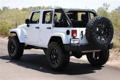 a white jeep with black wheels parked on the side of the road in front of some bushes