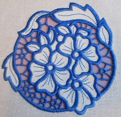 a blue doily with white flowers and leaves on the edge is sitting on a piece of fabric