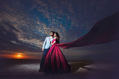 a man and woman standing on the beach at sunset