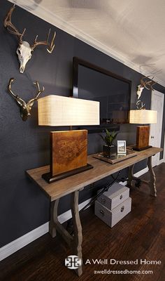 two deer heads are mounted on the wall above a table with lamps and other items