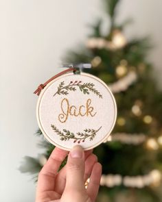 a person holding up a cross stitch ornament with the word jack on it