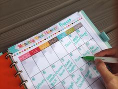 a person is writing on a planner with a green pen and orange notebook in front of them