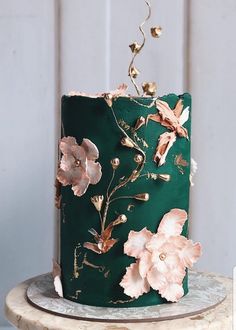 a green cake decorated with flowers and gold leaves on a marble stand in front of a white wall