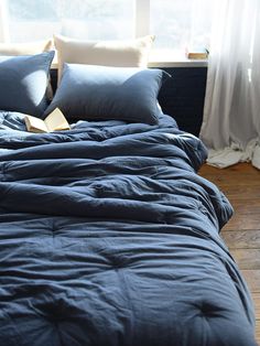 an unmade bed with blue sheets and pillows in front of a window overlooking the ocean