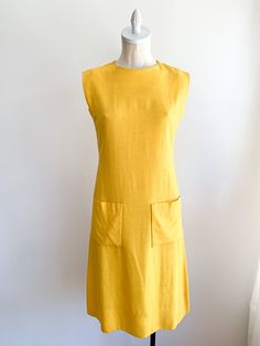 Happy yellow structured dress with subtle luxury detailing. Missing original belt. We suggest adding a rope or skinny belt for a modern update to complete this classic look. Front pockets and hidden back zip. Fabric: Linen blendLabel: Pauline TrigèreFit: SEra: 1960/70’s Measurements: Bust 34" Shoulder 16" Length 41" Waist 30" Hips 38" Condition: Very good. Very slight pulling at left arm seam (see photo). Yellow Sheath Midi Dress For Work, Yellow Midi Dress With Pockets, Yellow A-line Midi Dress For Work, Yellow Knee-length Dresses With Pockets, Chic Mustard Workwear Dress, Mustard Chic Dress For Work, Chic Mustard Dress For Work, Happy Yellow, Structured Dress