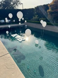 white balloons floating in the water near a swimming pool with lounge chairs and tables around it