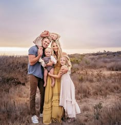 a man and woman with two children posing for a photo in a field at sunset