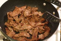 meat is being cooked in a frying pan on the stove top with a spatula