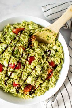 a white bowl filled with green pasta salad and a wooden spoon on top of it