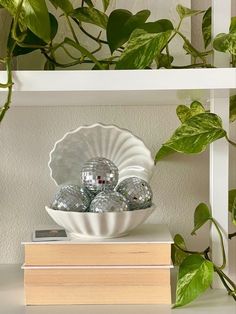 a white bowl filled with crystal balls sitting on top of a stack of books next to a green plant