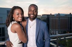 a man and woman standing next to each other on top of a roof with buildings in the background