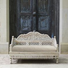 an old white bench sitting in front of a wooden door with ornate carvings on it