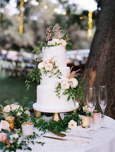 a white wedding cake sitting on top of a table next to wine glasses and candles