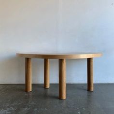 a round wooden table sitting on top of a cement floor next to a white wall