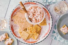 a plate with crackers, crackers and dip on it next to wine glasses