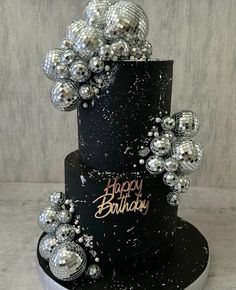 a three tiered black and silver birthday cake with disco balls on the top layer