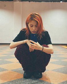 a woman sitting on the floor looking at her cell phone while holding it in her hands