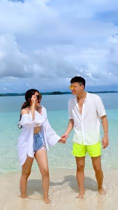 a man and woman holding hands while standing in the water on a beach next to each other