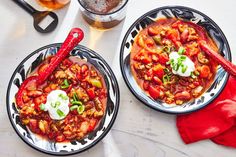 two bowls filled with chili and beans on top of a white table next to red napkins