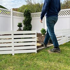 a man is walking in the grass near a fence and some plants on the ground