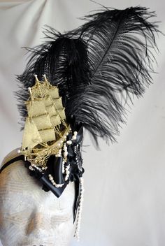 "Part of the Decadence Mini Collection,this dramatic rococo style headdress will add an original Marie Antoinette flair to your costume! Made in a royal black and gold color combination, this unique fascinator features two black ostrich feathers that flow over a golden galley ship. The whole piece is compleat with a \"sea\" of black blossoms and lush ivory pearls, black ribbon bows and a beautiful black cupid cameo, adorned with sparkling rhinestones. This mini hat is fully lined with satin and Vintage Black Costume Hats And Headpieces For Themed Events, Vintage Black Costume Hats For Themed Events, Gothic Black Hats And Headpieces For Themed Events, Gothic Black Costume Hats And Headpieces For Themed Events, Vintage Black Costume Hats And Headpieces For Carnival, Vintage Black Costume Hat For Carnival, Victorian Black Costume Hats And Headpieces For Costume Party, Black Victorian Costume Hat For Costume Party, Black Pirate Hat For Party