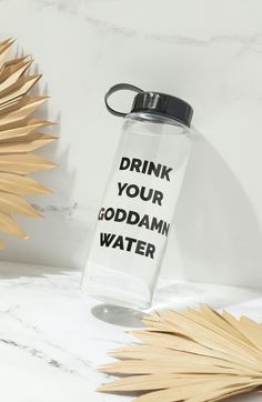 a water bottle with the words drink your god damn water on it next to palm leaves