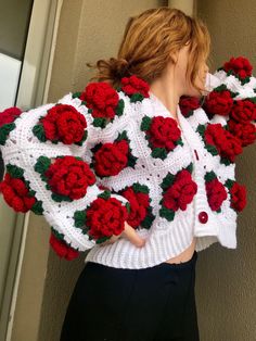 a woman wearing a white and red crochet jacket with roses on it,