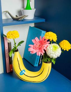 a banana shaped vase with flowers in it on a blue table next to some books