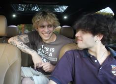 two young men sitting in the back seat of a car, one with tattoos on his arm