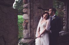 a bride and groom standing in front of an old stone structure with greenery around them