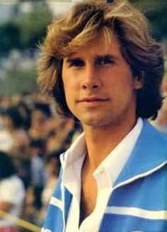 a man with long hair standing in front of a crowd wearing a blue and white shirt