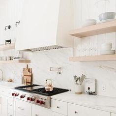 a kitchen with white cabinets and marble counter tops, open shelving above the stove