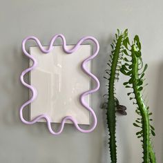 a pink and white wall mounted mirror next to a green plant