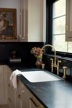 a kitchen sink sitting under a window next to a counter top with flowers on it