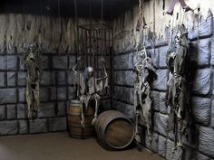 a room with several wooden barrels and statues hanging from the ceiling, in front of a brick wall