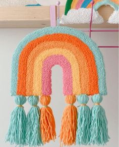 a rainbow rug hanging on a wall with tassels around it and a crochet hook